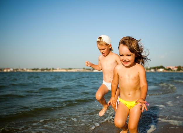 Happy little girl and boy running on water edge in sunshine