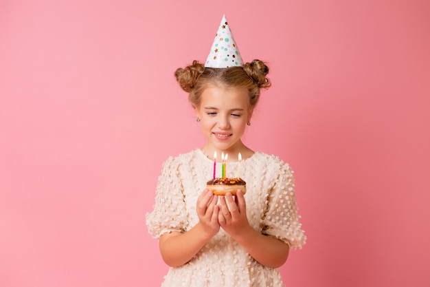 Happy little girl in a cap for her birthday makes a wish and blows out candles on a cake.