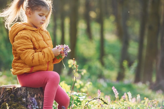 Happy little girl in casual clothes sitting in spring forest at daytime