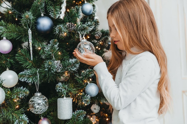 幸せな少女は家でクリスマスツリーを飾ります。冬の休日と人々の概念