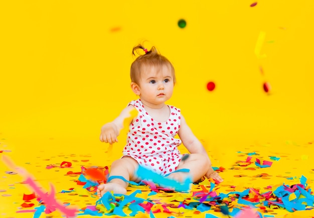 Happy little girl in a dress in peas catches confetti on a yellow background. place for text