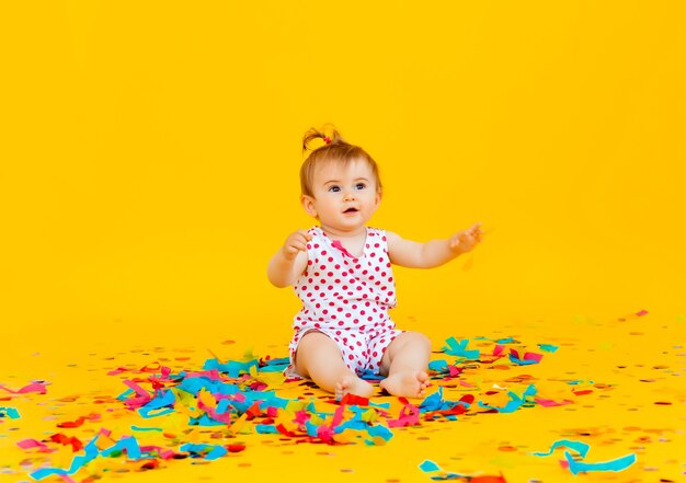 Happy little girl in a dress in peas catches confetti on a yellow background. place for text