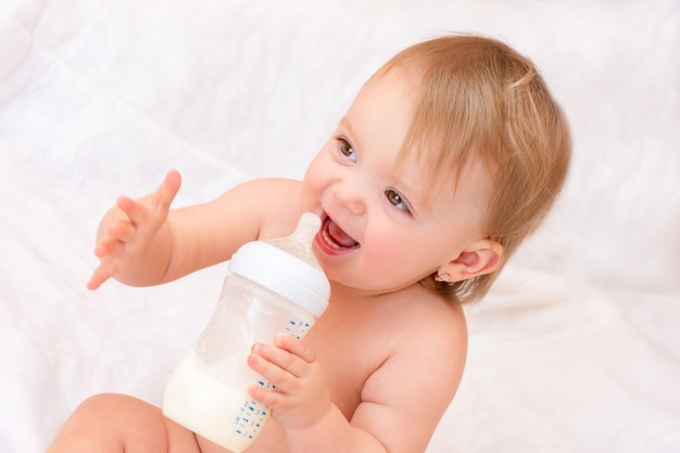 Happy little girl drinks milk from a bottle