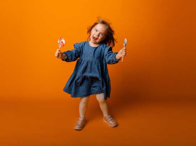 大きなロリポップを食べる幸せな少女、キャンディーを持つ子供。明るい背景、スタジオで隔離。