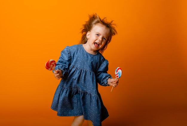 Счастливая маленькая девочка ест большой леденец на палочке, ребенок с конфетой. изолированные на ярком фоне, студия.