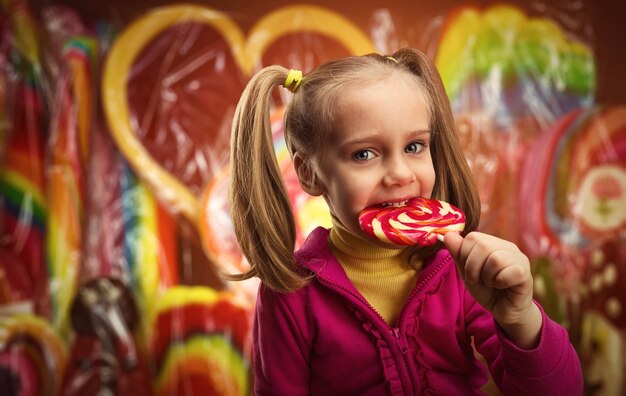 Happy little girl eating lollipop over multicolored surface