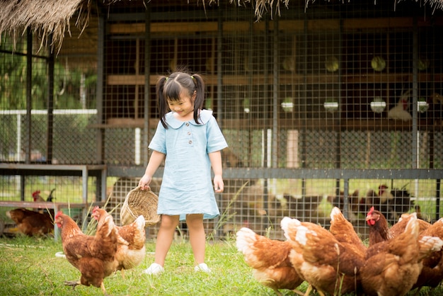 닭 농장 앞에서 닭을 먹이 행복 한 작은 소녀.
