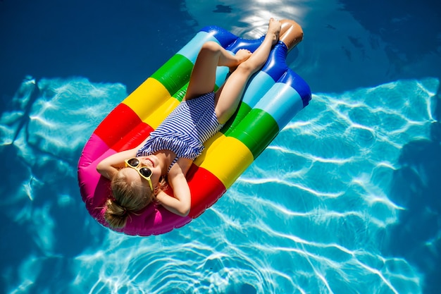 happy little girl floating on a mattress in the pool