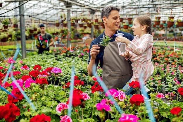 Happy little girl having fun while water flowers with her father at plant nursery