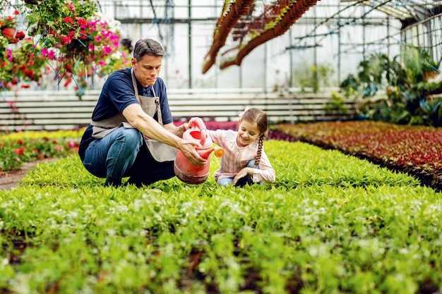 Happy little girl having fun while watering plants and helping her father at garden center