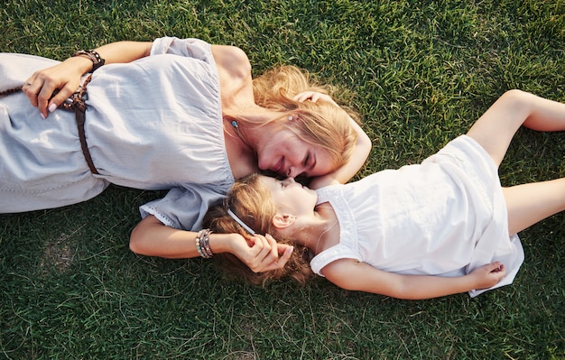 Happy little girl and her mother having fun outdoors on the green grass in sunny summer day