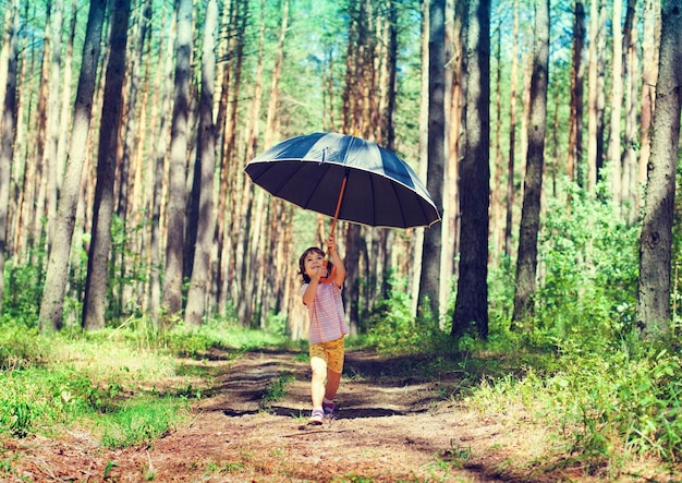 Happy little girl hiding under big black umbrella in fair weather