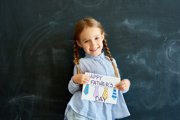 Фото Счастливая маленькая девочка держит открытку на день отцов