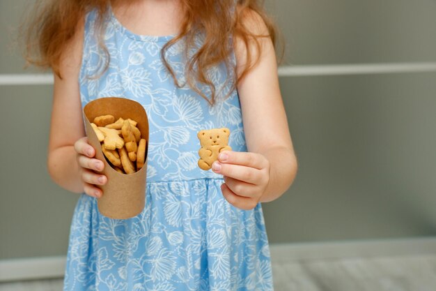 自家製のカーリークッキーの紙のカップを持った幸せな小さな女の子学校の食事
