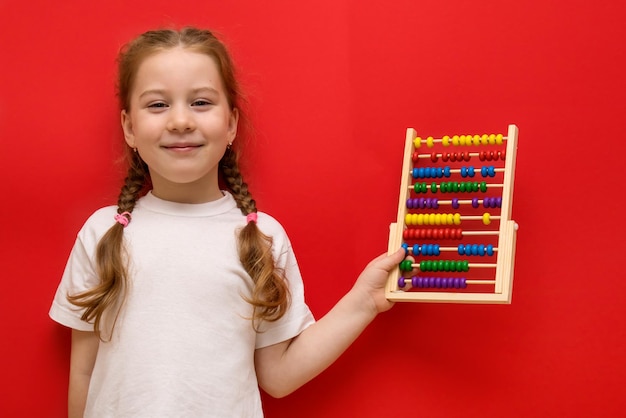 Happy little girl holds abacus in hands On red background