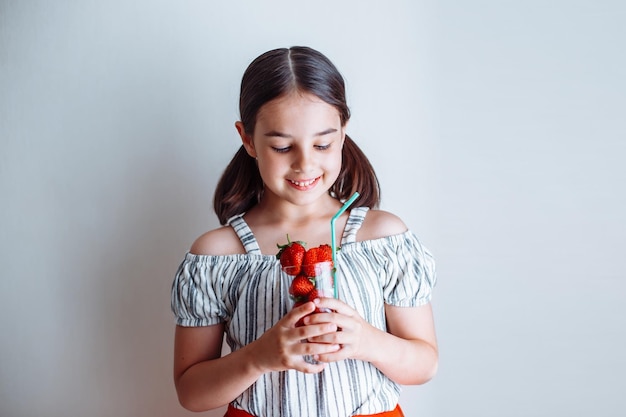 A happy little girl holds a glass with fresh strawberries