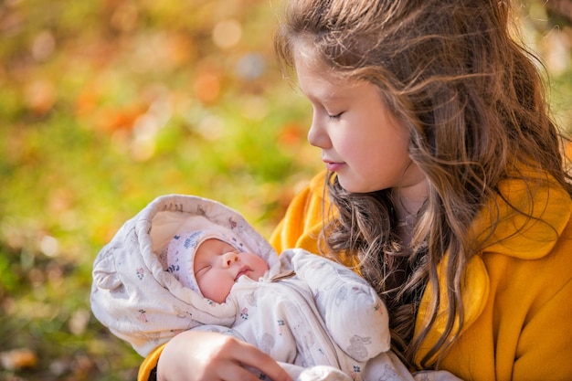 Happy little girl hugging her newborn sister in the autumn park on a sunny day