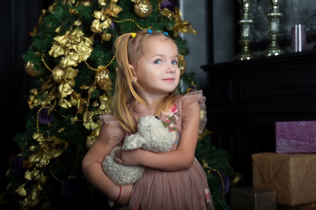 Happy little girl hugs her favorite toy in the room decorated for Christmas
