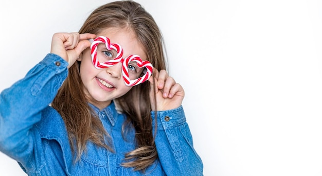 사진 카라멜 안경을 쓴 행복한 어린 소녀는 하트와 미소로 카메라를 쳐다보고 있습니다. 발렌타인 데이 배경 텍스트 복사 공간
