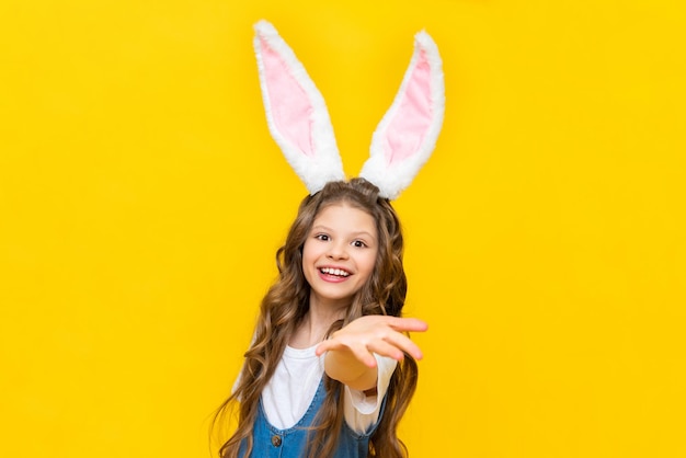 행복한 어린 소녀가 아이들을 위한 부활절 봄 휴가를 즐기고 있습니다 긴 귀를 가진 토끼 옷을 입은 아이 노란색 외진 배경에 곱슬머리를 한 매력적인 여성