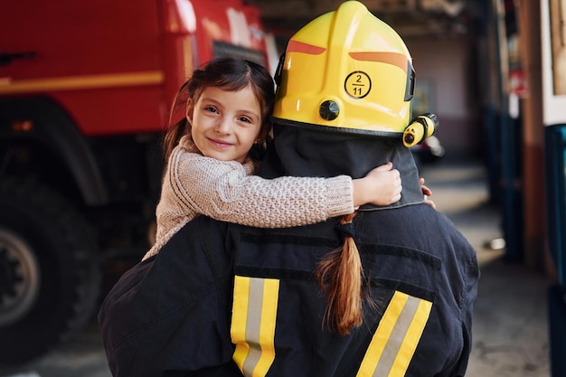 Happy little girl is with female firefighter in protective uniform