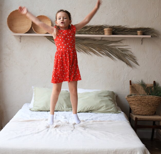 행복한 어린 소녀가 침대에 뛰어올라 노래를 부르고 있습니다.