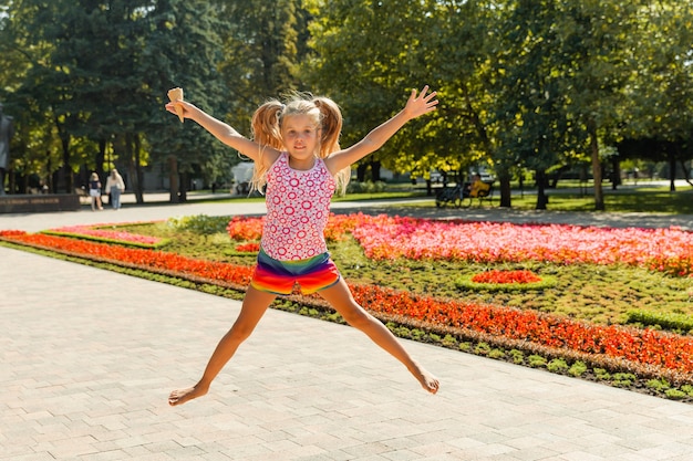 Bambina felice che salta nel parco. bambina che mangia il gelato e si diverte in città.