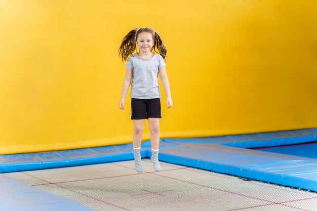 Happy little girl jumping on trampoline in fitness center