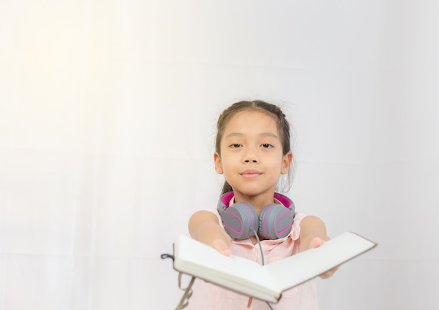 Happy little girl kid standing with headphones and hand holding book