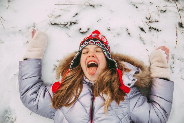 ニット帽をかぶった幸せな少女は雪と笑顔に横たわっています。上からの眺め