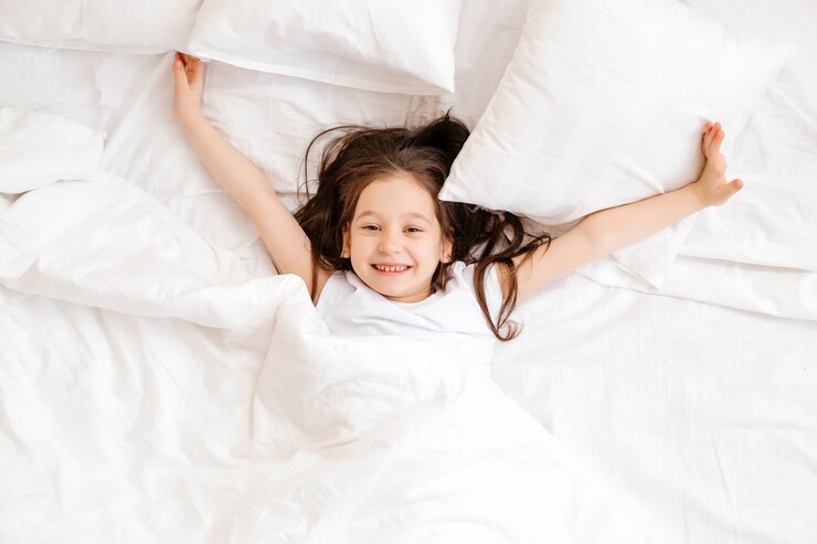 Photo happy little girl lies in bed at home in the morning. healthy baby sleep. white bed linen, space for text