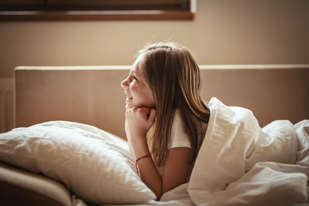 A happy little girl lies on the bed in the morning and laughs after awakening.