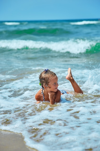 Счастливая маленькая девочка лежит на берегу моря в волнах