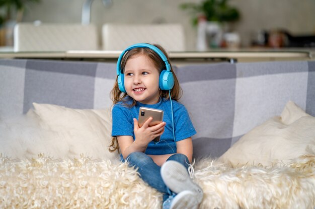 Happy little girl listening to music in blue headphones, at home