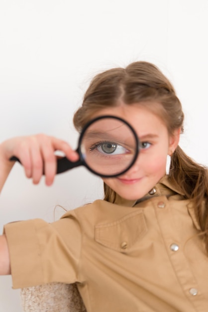 Happy little girl looks through a magnifying glass on a light background. Research, discovery