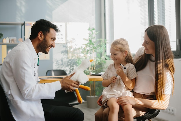 Photo happy little girl mother and family doctor playing fun game with toy and neurologists hammer