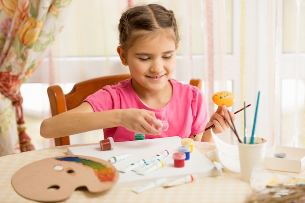 Happy little girl painting eggs for Easter