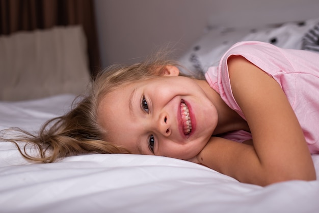 A happy little girl in pajamas is lying on the bed in the bedroom