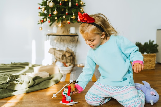 パジャマ姿の幸せな少女がクリスマスのおもちゃで遊んでいる鹿鹿子供はクリスマスの飾りで飾られた部屋で遊んでいます。メリークリスマスと新年あけましておめでとうございますのコンセプト。家族の居心地の良い瞬間