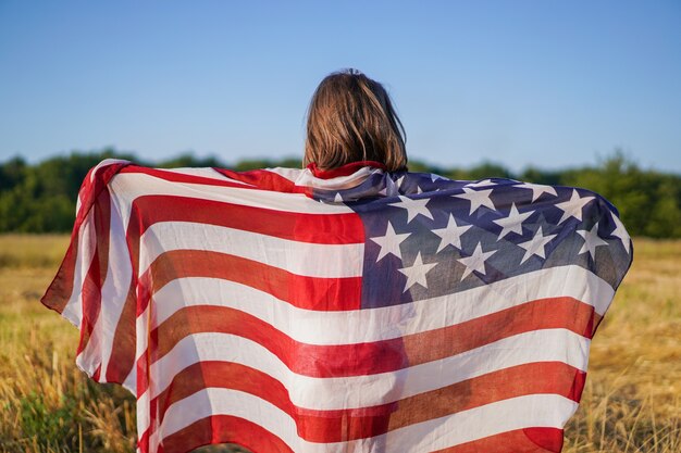 Foto patriota felice della bambina che corre nel campo con la bandiera americana.