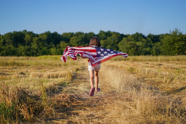 Happy little girl patriot running in the field with American flag.