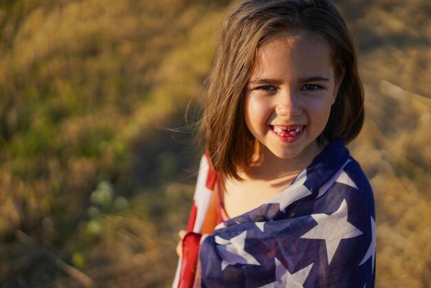 Happy little girl patriot running in the field with american flag