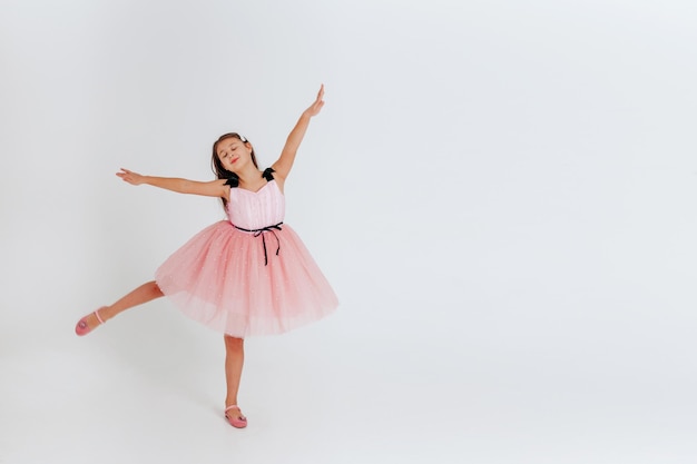 Happy little girl in pink dress dancing on a white background Space for text