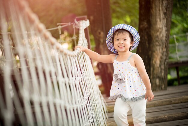 Happy little girl playing climbing on the rope bridge.