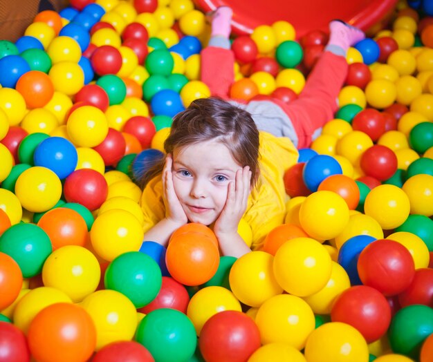 Happy little girl playing in colorful balls. Happy child playing at colorful plastic balls in play center