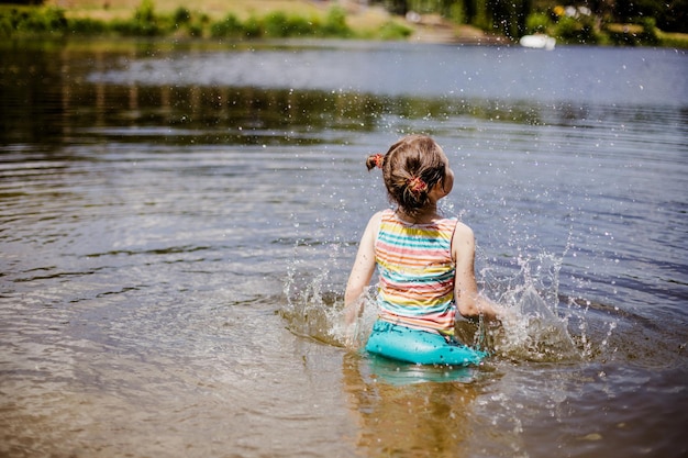 夏の日に湖で遊ぶ幸せな少女少女は水に手を上げて水滴をはねかける