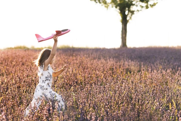 Happy little girl playing with airplane on a lavender field during sunset children play toy airplane