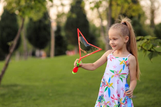 Happy little girl playing with summer soap bubbles in the park.