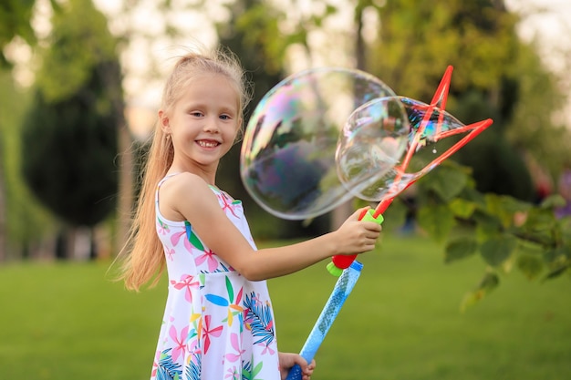 Happy little girl playing with summer soap bubbles in the park.