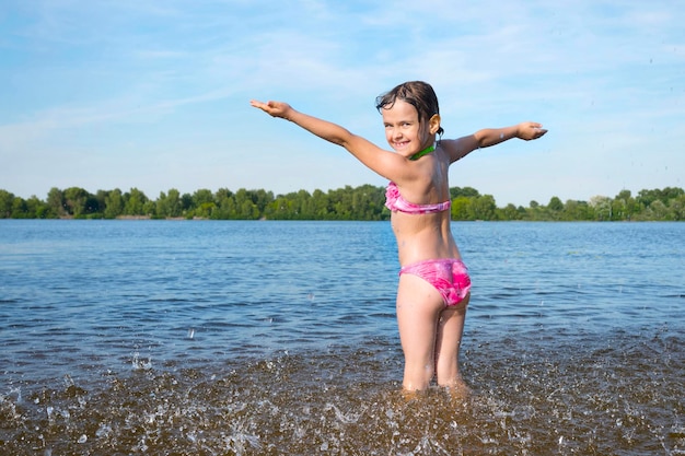 Happy little girl playing with water on the river bank on a sunny day